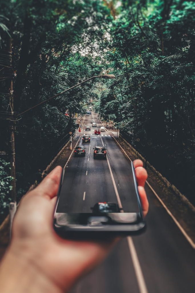 Creative blend of technology and nature with smartphone framing a bustling road through forest.
